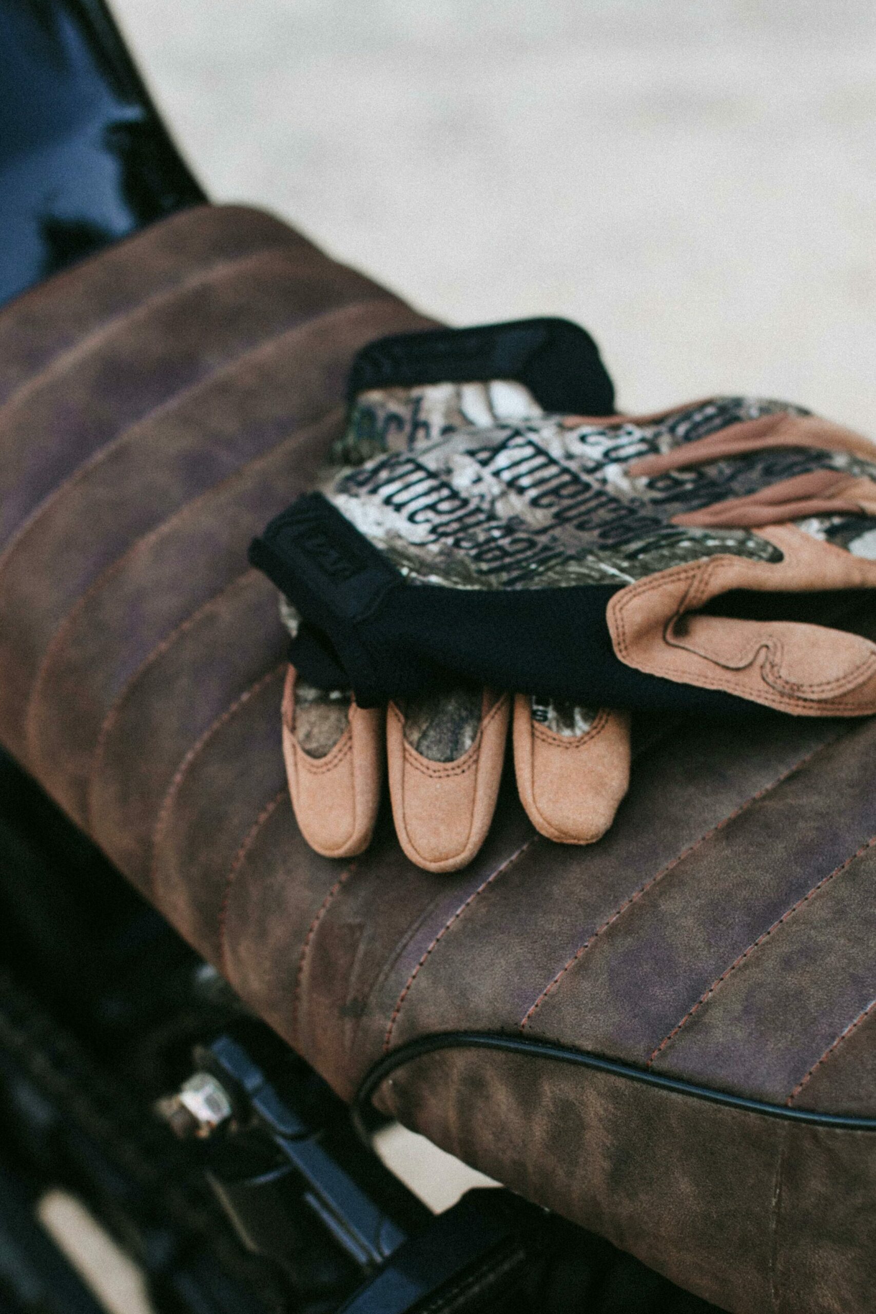 Leather gloves resting on a classic motorcycle seat in an outdoor setting, embodying adventure.